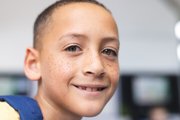 Biracial boy with freckles smiles warmly in a school classroom, his brown eyes gleaming