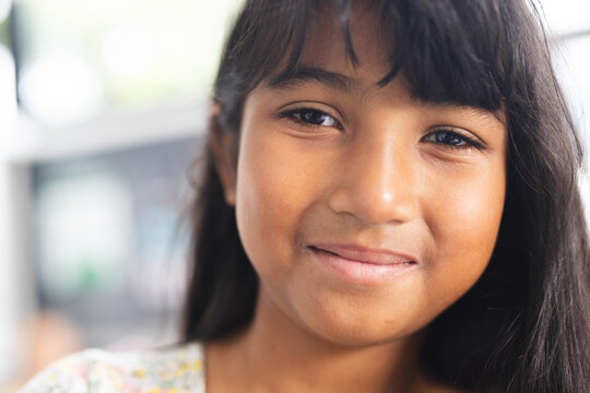 Biracial girl with a gentle smile, her dark hair falls softly around her face in a school classroom