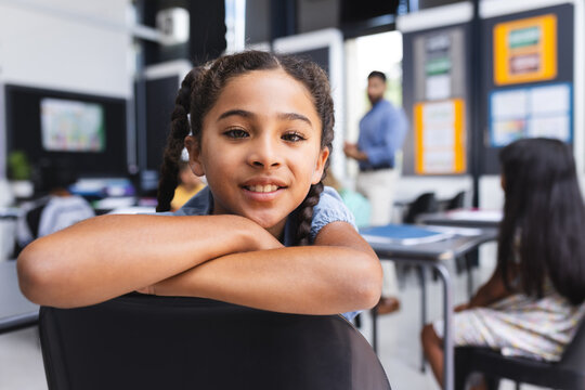 Biracial girl with braided hair smiles in a school classroom