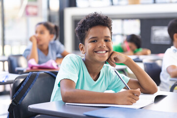 In school, young biracial boy with curly hair is writing in the classroom