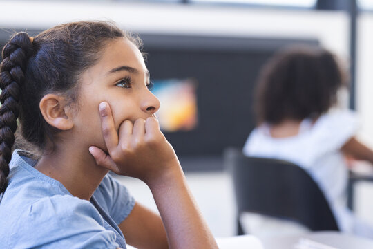 Biracial girl with braids appears thoughtful in a classroom, embodying th