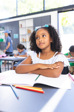 A biracial girl with curly hair sits at desk, deep in thought