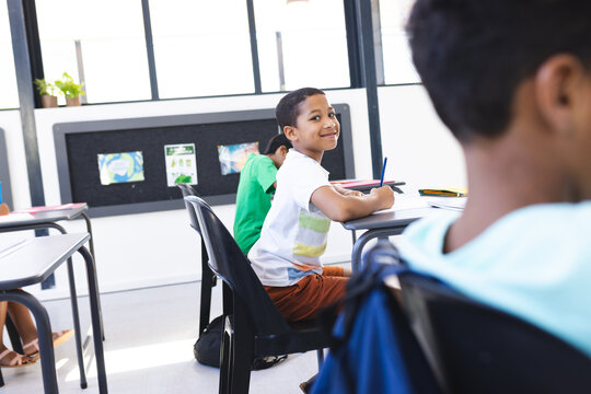 Biracial boy smiles, looks back at classmate in school classroom