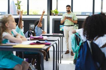 In school, young students are raising hands, Asian male teacher standing