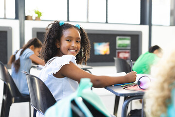 A biracial girl in white dress smiles in a classroom