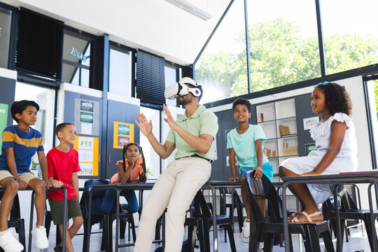 In school, Asian male teacher wearing VR headset is explaining to diverse students
