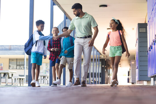 In school, Asian male teacher walks with three biracial boys and girl