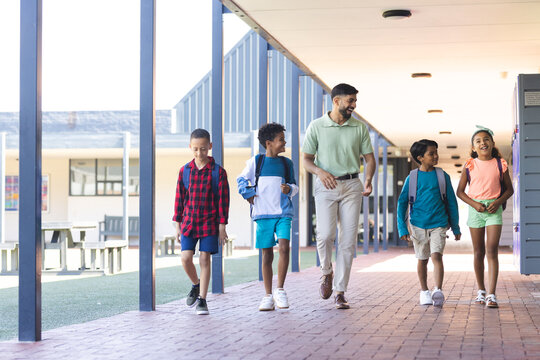 In school, diverse group of young students walking with their Asian teacher