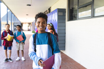 Biracial boy with a bright smile stands in a school hallway, holding a folder