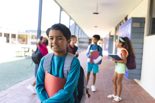 Biracial boy with a striped shirt holds a red folder, smiling at school