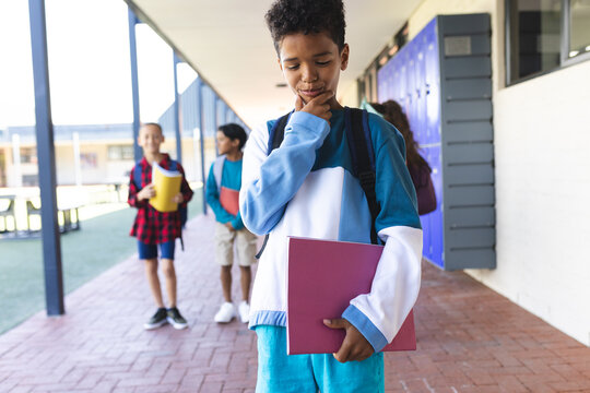 Biracial boy in blue stands thoughtfully in a school corridor, holding a book