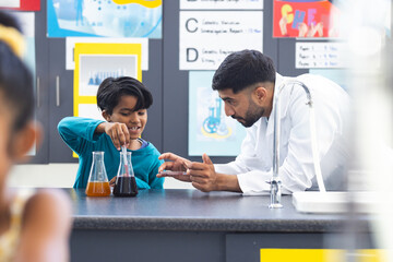 In school, Asian male teacher guiding biracial male student in doing a science experiment
