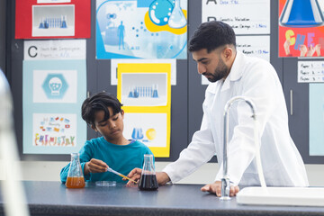Young Asian male teacher assists biracial boy with a science experiment in school