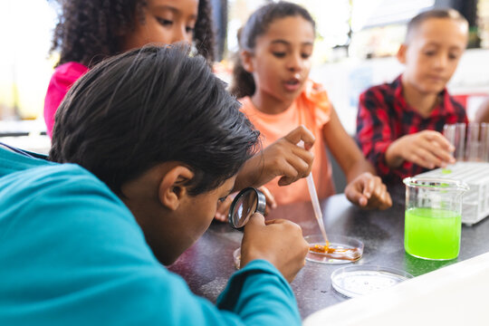 Biracial children do a school science experiment, one using a magnifying glass