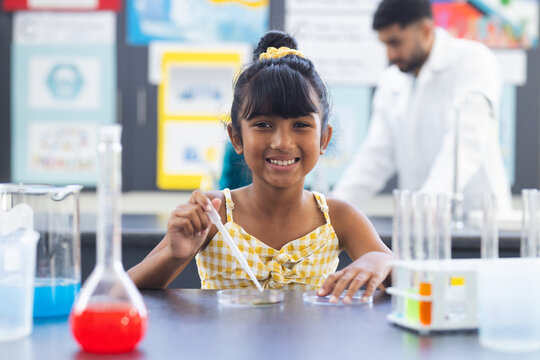 Biracial girl in yellow conducts experiment, male scientist watches