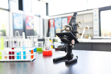 A microscope sits on a table surrounded by colorful test tubes and beakers in school