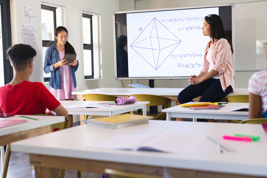 Young biracial female teacher teaches geometry in a bright high school classroom