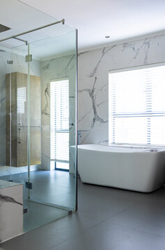 At home, glass shower and white bathtub are dominating a modern bathroom