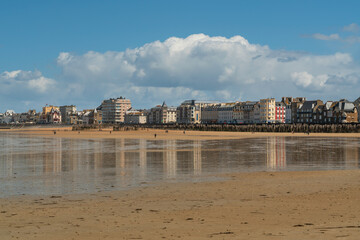 View of the promenade and the beach with wooden breakwaters at low tide on a sunny summer day,...