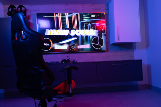 At home, gaming chair facing a large screen displaying HIGH SCORE
