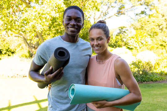 A diverse young couple holding yoga mats, smiling outside