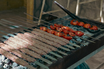 Iraninan kebab named Koobideh or minced lamb on skewers next to some tomatoes on charcoal fire being barbecued 