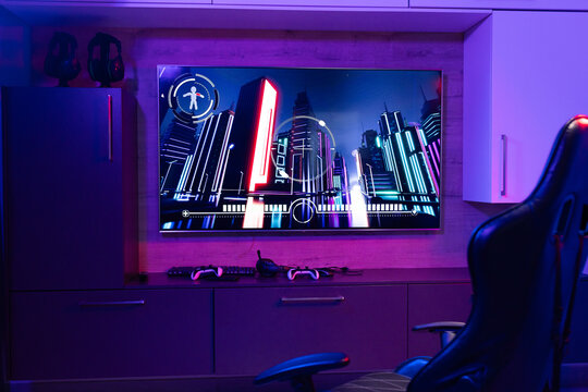 At home, facing neon cityscape art on a purple glow, seated in a gaming chair