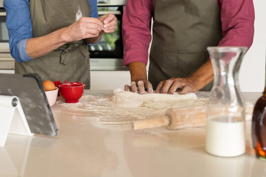 At home, diverse senior couple in aprons baking together in kitchen
