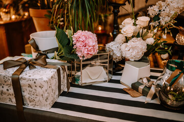 Riga, Latvia, - August 26, 2023 - Elegant table setting with wrapped gifts, pink and white flowers, and decorative items on a black-and-white striped tablecloth in an indoor setting...