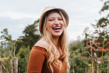 Latin woman with blonde hair, hat and white skirt, happy in nature surrounded by trees. Woman in the countryside enjoying her holidays.