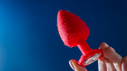Woman holding red anal plug in water drops on blue background. 