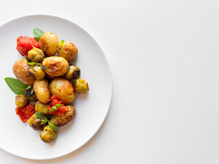 Roasted baby potatoes and Brussels sprouts with cherry tomatoes on white plate, garnished with basil, healthy vegetarian dish concept with space for text.