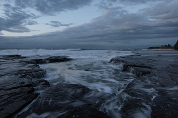 Wave water flowing into the rocky channel in a cloudy morning.