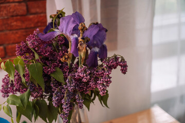 Withered bouquet of lilac and iris flowers in a glass vase.