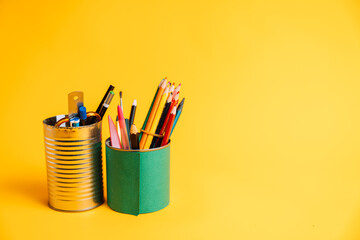 Recycling tin cans for containers with pencils and pens on yellow background.