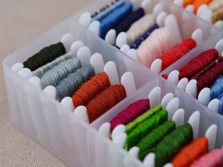 Plastic sorting box full of bobbins with different colour embroidery threads on a beige canvas...