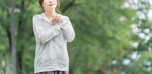 公園で準備体操・ストレッチするスポーツウェアのアジア人女性
