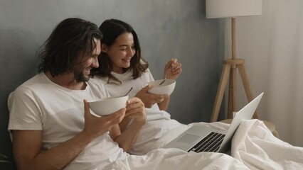A couple enjoys breakfast in bed while watching something on a laptop, capturing a cozy morning routine. Cinematic slow motion 4k footage, design for advertising, and social media, vlog - Powered by Adobe