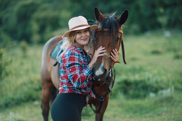 Obraz premium Happy blonde with horse in forest. Woman and a horse walking through the field during the day. Dressed in a plaid shirt and black leggings.