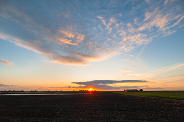 The sun sets, still casting its colorful light on the clouds above the Dutch landscape