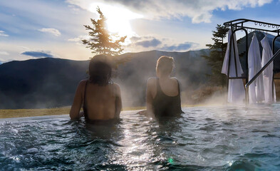 Spa on holidays. Two young women relaxing in outdoor hot pool. Mountain view