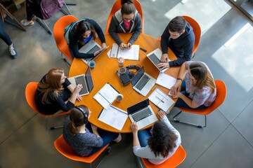 Collaboration in modern workspace involves a team meeting around a round table with laptops and notes. It is a setting for teamwork, discussion, and brainstorming among professionals using technology