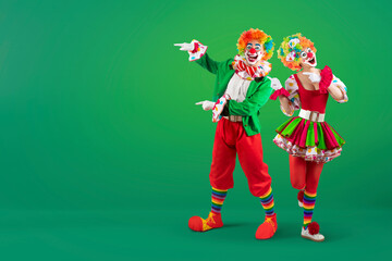 Funny clowns pointing at blank template copy spase for advertising, posters, greetings, invitations. Entertainer as Joker in a suit and wig, with clown whiteface makeup © TSViPhoto