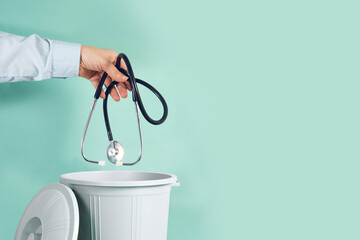 Hand throwing stethoscope into trash bin or waste bucket. Quitting medical profession concept
