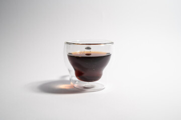 A glass of dark liquid sits on a white background. The liquid appears to be coffee or tea, and the cup is made of glass. Concept of calm and relaxation