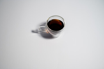 A cup of coffee is sitting on a white table. The cup is half full and the coffee is dark. Concept of relaxation and comfort, as coffee is often associated with taking a break