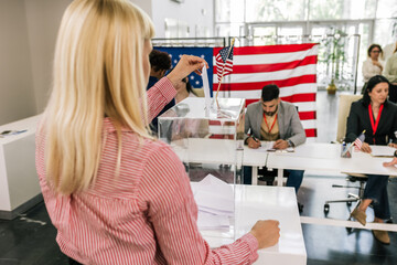 Young woman voter placing ballot in ballot box polling place in America.