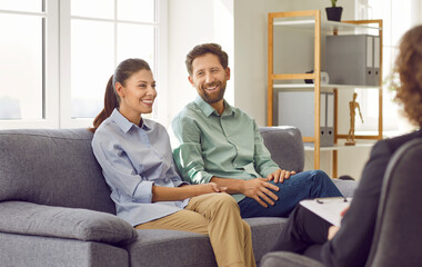 Cheerful family couple having a psychotherapy session. Happy man and woman sitting together on the sofa and discussing their marriage and relationship with their therapist. Therapy concept