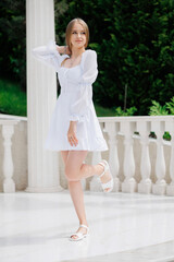 A woman in a white dress is posing for a photo. She is wearing a necklace and has her hair in a...