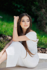 Naklejka premium A woman in a white dress is sitting on a stone ledge. She has her arm around her waist and is smiling